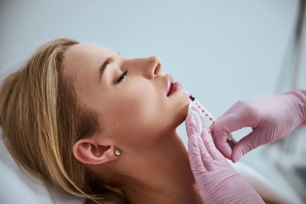 Professional cosmetologist injecting a dermal filler into the patient lips Home